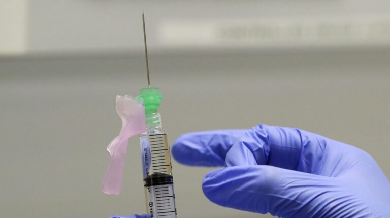 A gloved finger prepares the COVID-19 vaccine to administer to a volunteer.