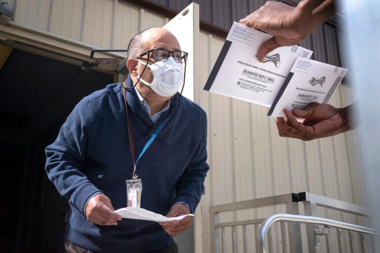 An employee of the Philadelphia Commissioners Office examines ballots at a satellite election office at Overbrook High School on Thursday, Oct. 1, 2020, in Philadelphia. (AP Photo/Laurence Kesterson)