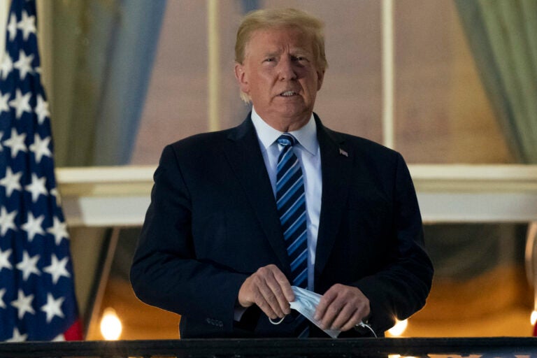 President Donald Trump removes his mask as he stands on the Blue Room Balcony upon returning to the White House Monday, Oct. 5, 2020, in Washington, after leaving Walter Reed National Military Medical Center, in Bethesda, Md. (AP Photo/Alex Brandon)