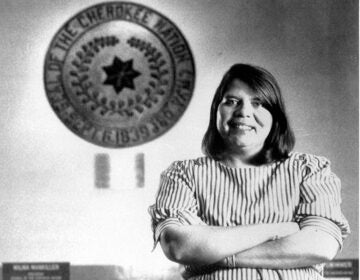 Black and white photography of Wilma Mankiller in front of the tribal emblem at the Cherokee Nation