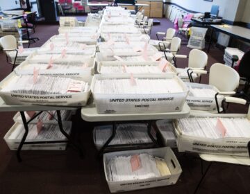 A table full of boxes of mail-in ballots is visible.