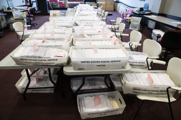 A table full of boxes of mail-in ballots is visible.