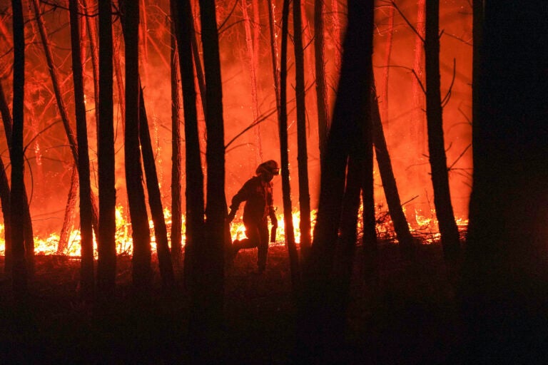A firefighter is silhouetted against a fire burning outside the village of Roqueiro