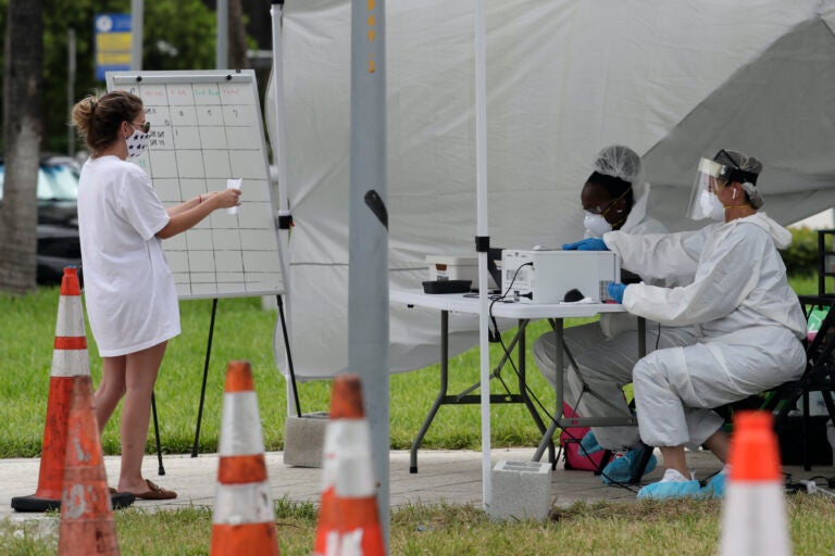 Health care workers take information from people in line at a walk-up COVID-19 testing site