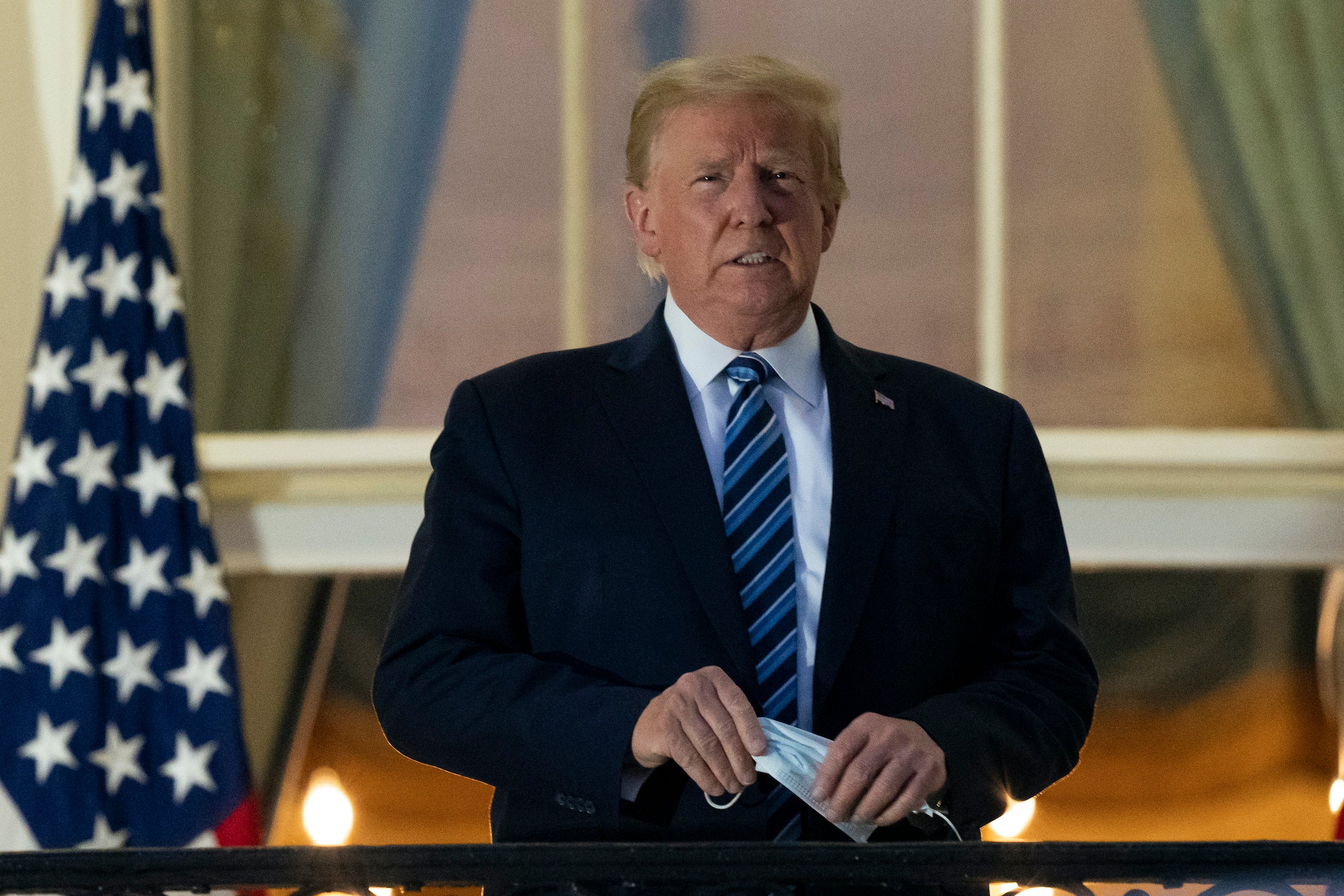 President Donald Trump removes his mask as he stands on the Blue Room Balcony