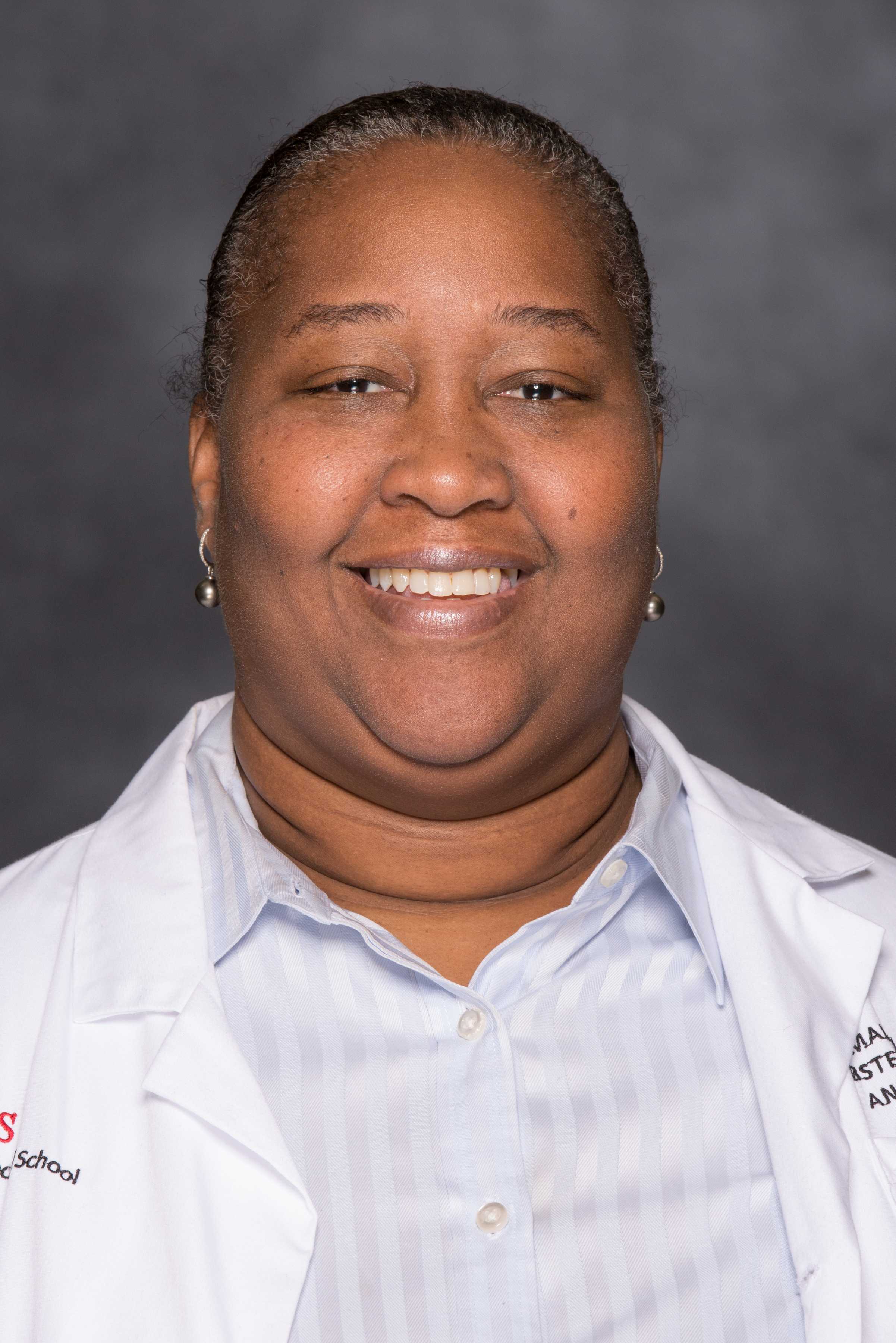 Dr. Damali Campbell, a Black woman, in a lab coat and blue button down shirt.