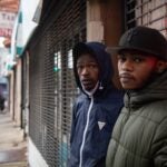 Two young Black men standing in front of a storefront.