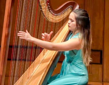 Claire Thai wearing a teal dress playing the harp on stage