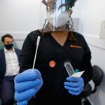 A medical assistant holds a swab after testing a man on Wednesday at the new COVID-19 testing facility at Boston Logan International Airport. (Elise Amendola/AP Photo)