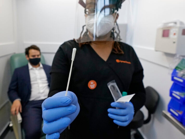 A medical assistant holds a swab after testing a man on Wednesday at the new COVID-19 testing facility at Boston Logan International Airport. (Elise Amendola/AP Photo)