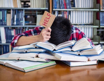 A tired and stressed student with his head down on a pile of books holding up a 