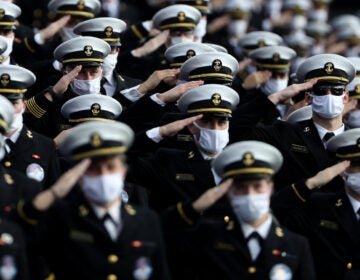 Midshipmen wearing face masks stand and salute.