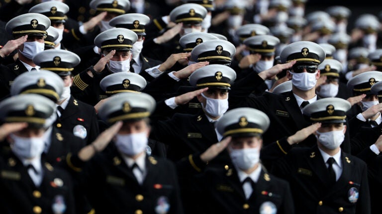 Midshipmen wearing face masks stand and salute.