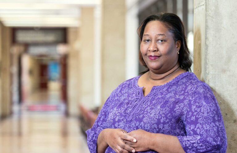 Dr. Damali Campbell-Oparaji, a Black woman, wearing a purple shirt stands in a hallway.