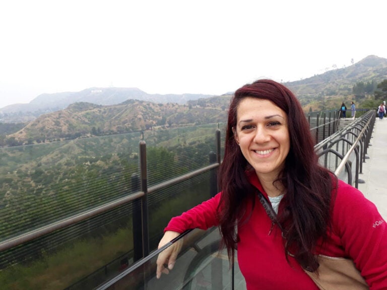 Woman with long reddish hair and a red shirt smiles by a scenic overlook