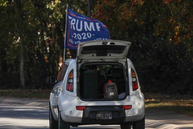 A Trump supporter drives by a polling location while holding a Trump 2020 flag as the national anthem plays from the back of his vehicle on election day Tuesday, Nov. 03, 2020, at Thurgood Marshall elementary  school in Newark, Del. (Saquan Stimpson for WHYY)