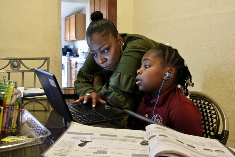 Yolanda Biggers helps her daughter, Zyiah Satterwhite, 7, find her assignment.  After the coronavirus pandemic hit, Biggers gave up her shifts as a part-time nurse to focus all of her attention on Zyiah and her two older sisters as they adapted to virtual schooling. (Emma Lee/WHYY)