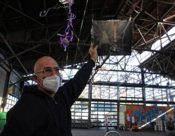 John Schlesinger holds a still life painting, broken and repaired, up to the light at the Cherry Street Pier. The work produces the desired effect when lit from behind. (Emma Lee/WHYY)