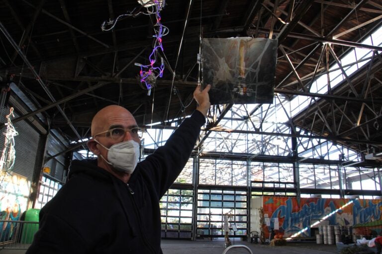 John Schlesinger holds a still life painting, broken and repaired, up to the light at the Cherry Street Pier. The work produces the desired effect when lit from behind. (Emma Lee/WHYY)