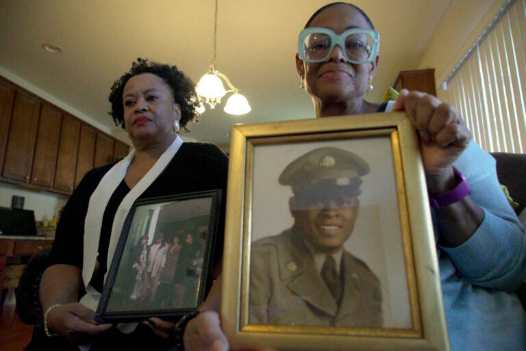 Sisters Barbara Leak-Watkins, right, and Alberta Lynn Fantroy pose with photos of their late father, Alex Leak Jr., at Watkins’ home in Greensboro, N.C., on Wednesday, Nov. 4, 2020. The Army veteran died in July after collapsing from dehydration at his assisted living facility, and the family believe pandemic-related neglect is to blame. (AP Photo/Allen G. Breed)