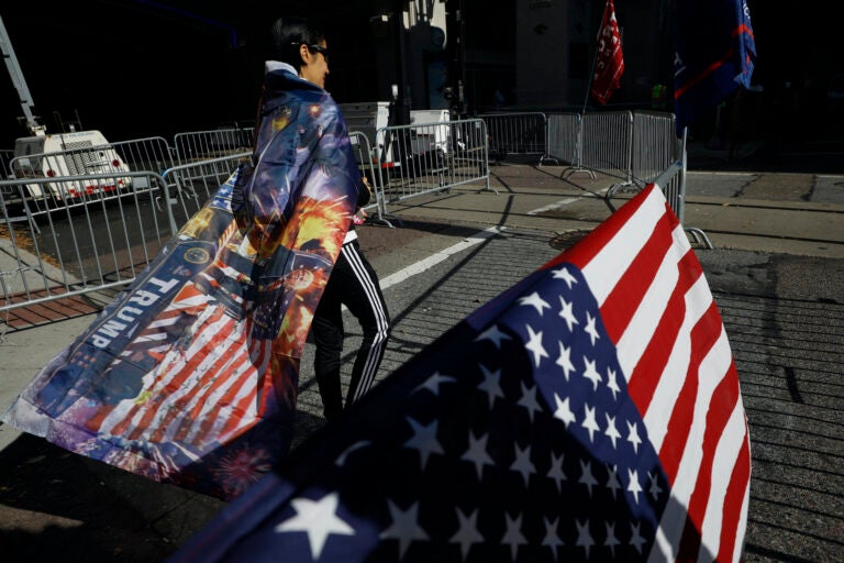 A woman wears a Trump flag as a cape as supporters of President Donald Trump protest outside the Pennsylvania Convention Center, where vote counting continues, in Philadelphia, Monday, Nov. 9, 2020, two days after the 2020 election was called for Democrat Joe Biden. (AP Photo/Rebecca Blackwell)