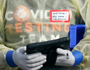 A worker wearing gloves, and other PPE holds a tablet computer as he waits to check people in, Wednesday, Oct. 28, 2020, at a King County coronavirus testing site in Auburn, Wash., south of Seattle. (AP Photo/Ted S. Warren)