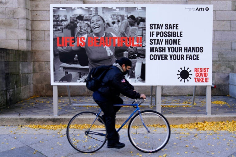 A man wearing a face mask bicycles along Broad Street, Wednesday, Nov. 18, 2020, in Philadelphia. (AP Photo/Matt Slocum)