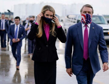 FILE- In this July 15, 2020, file photo Sen. Kelly Loeffler, R-Ga., puts on a face mask as she walks with Sen. David Perdue, R-Ga., right, at UPS Hapeville Airport Hub in Atlanta. (AP Photo/Evan Vucci, File)