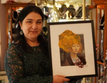 Ylvia Asal holding up a piece of her artwork in her Anatolia Art & Craft Studio. (Kenny Cooper/WHYY)