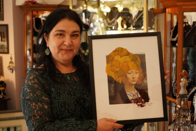 Ylvia Asal holding up a piece of her artwork in her Anatolia Art & Craft Studio. (Kenny Cooper/WHYY)