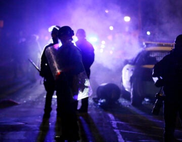 Police officers watch protesters as smoke fills the streets in Ferguson, Mo.