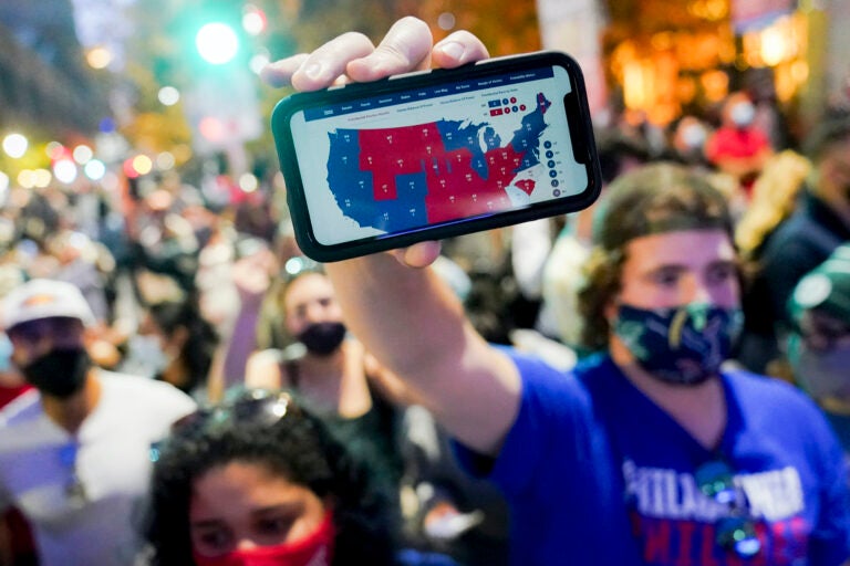 A supporter of President-elect Joe Biden holds up his mobile phone to display the electoral college map outside the Philadelphia Convention Center