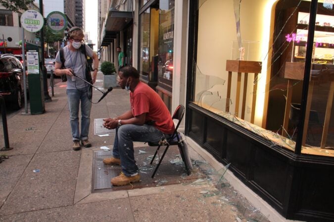 Peter Crimmins interviews Charles Lyons, who sat amid shattered glass in front of the Eyesite store on 18th Street armed with a hammer to discourage looters. (Emma Lee/WHYY)
