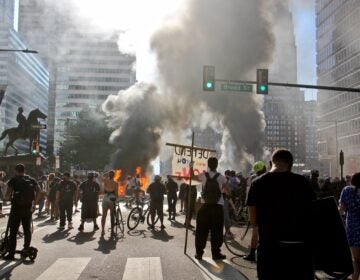 Smoke from burning police cars rises over protesters at Broad Street and JFK Boulevard. (Emma Lee/WHYY)