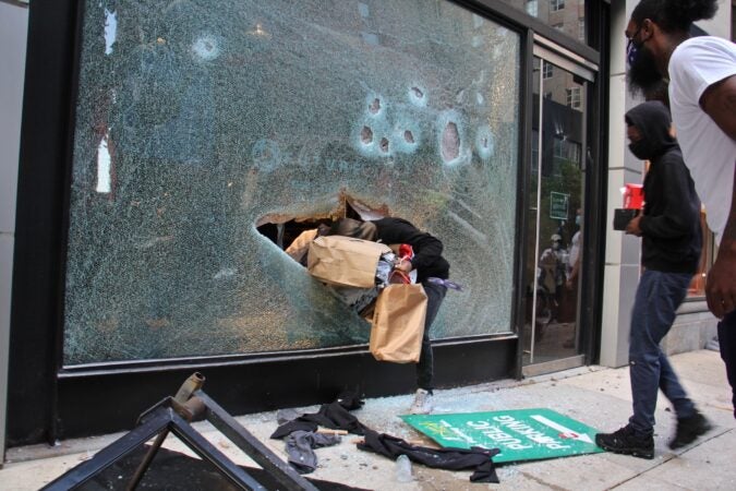 A looter emerges from the shattered window of a North Face store on Walnut Street in Philadelphia, May 30, 2020. (Emma Lee/WHYY)