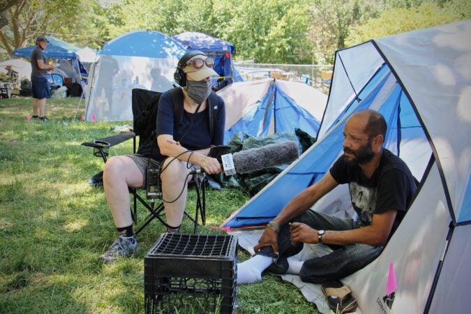 Susan Phillips interviews Jose Alicia at a protest encampment on the Ben Franklin Parkway. (Emma Lee/WHYY)