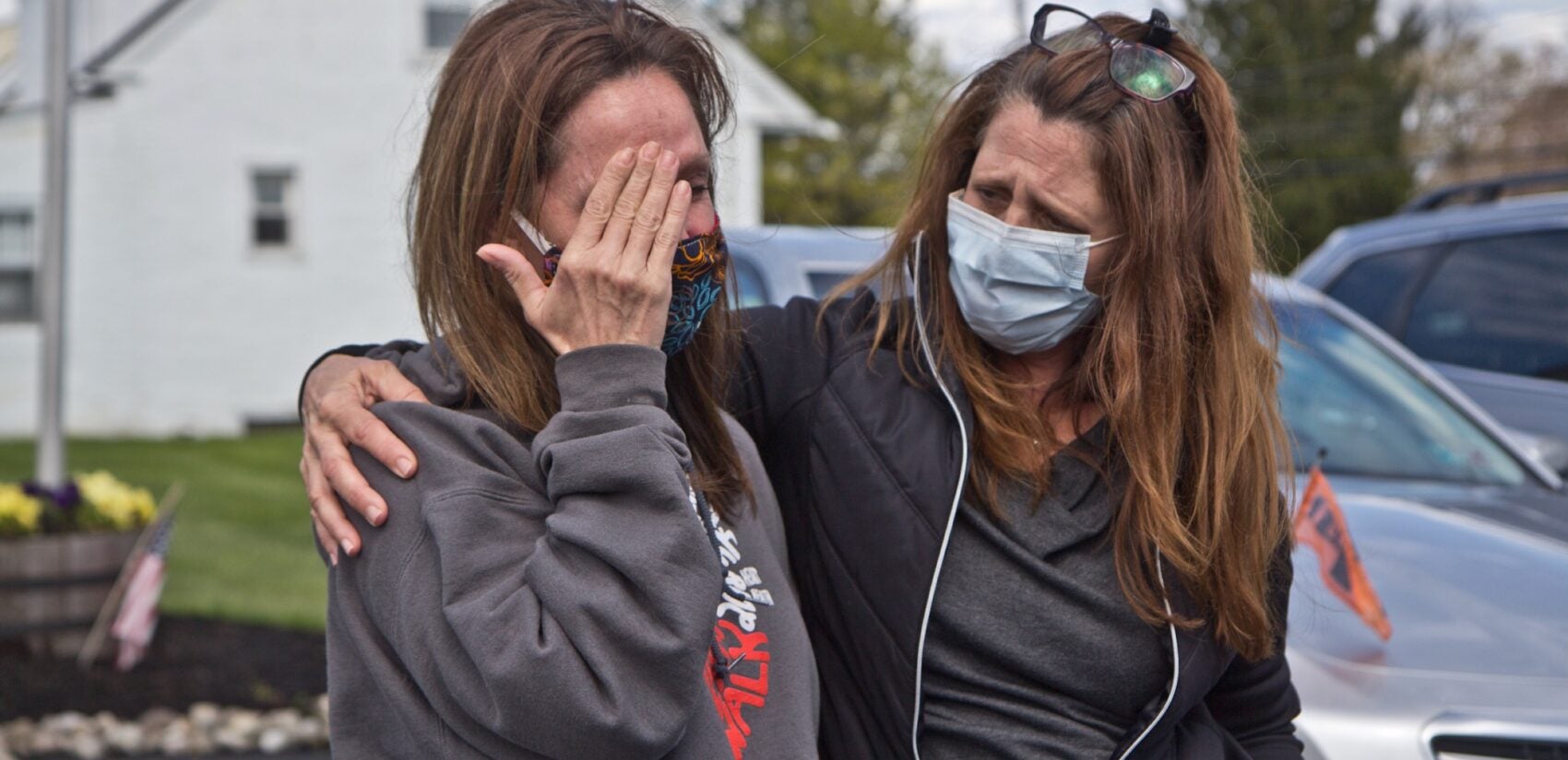 Tammy King (left) is comforted by her sister Michelle Rouco, both nurses, who were not allowed to see their father before he succumbed to COVID-19. (Kimberly Paynter/WHYY)