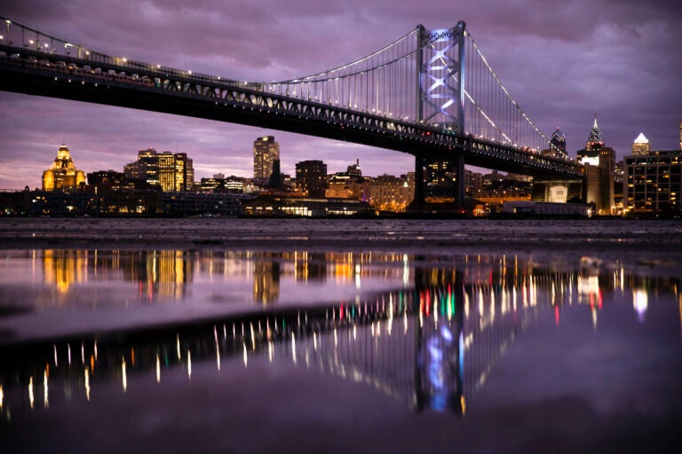 The Benjamin Franklin Bridge spanning the Delaware River between Camden N.J., foreground, and Philadelphia is reflected the mud revealed amid low and high tide, Thursday, Dec. 5, 2019. (AP Photo/Matt Rourke)