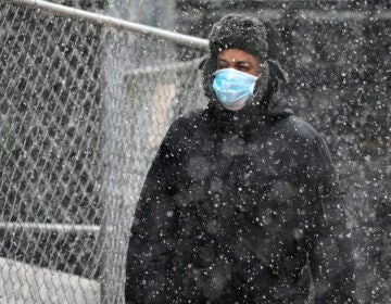 A man wearing a mask walks through a mid-afternoon snow squall in downtown Pittsburgh on Tuesday, Nov. 17, 2020. (AP Photo/Gene J. Puskar)