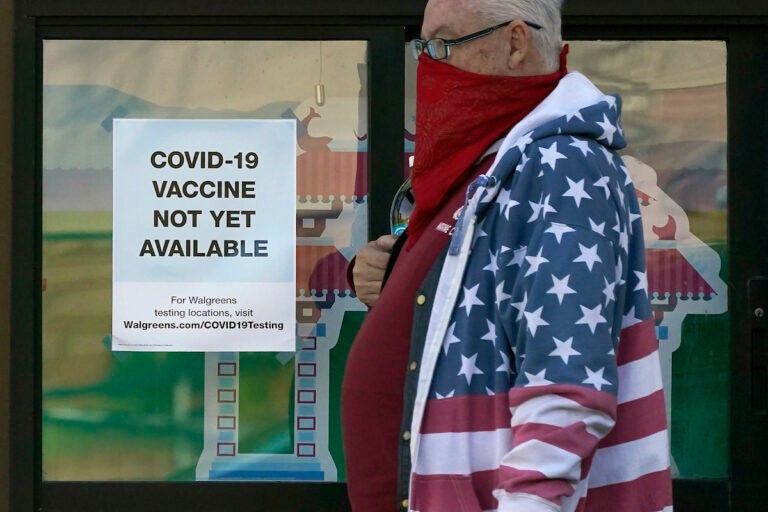 A pedestrian wearing a mask walks past a sign advising that COVID-19 vaccines are not available yet at a Walgreen’s pharmacy store during the coronavirus outbreak in San Francisco, Wednesday, Dec. 2, 2020. (AP Photo/Jeff Chiu)