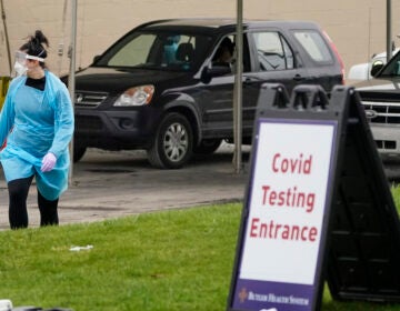 A health care worker walks past some of the vehicles lined up for COVID-19 testing at a drive-thru site, Friday, Dec. 4, 2020, in Butler, Pa. (AP Photo/Keith Srakocic)