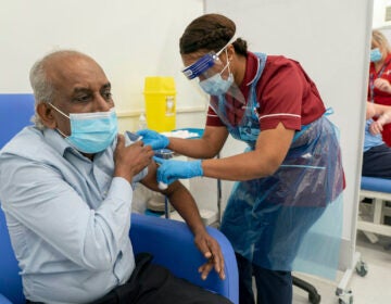 Care home worker Pillay Jagambrun, 61, receives the Pfizer/BioNTech COVID-19 vaccine in The Vaccination Hub at Croydon University Hospital in London, on the first day of the largest immunization program in the UK's history, Tuesday Dec. 8, 2020. (Dan Charity/Pool via AP)