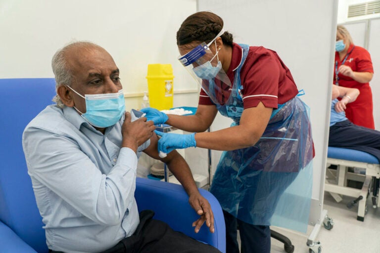Care home worker Pillay Jagambrun, 61, receives the Pfizer/BioNTech COVID-19 vaccine in The Vaccination Hub at Croydon University Hospital in London, on the first day of the largest immunization program in the UK's history, Tuesday Dec. 8, 2020. (Dan Charity/Pool via AP)