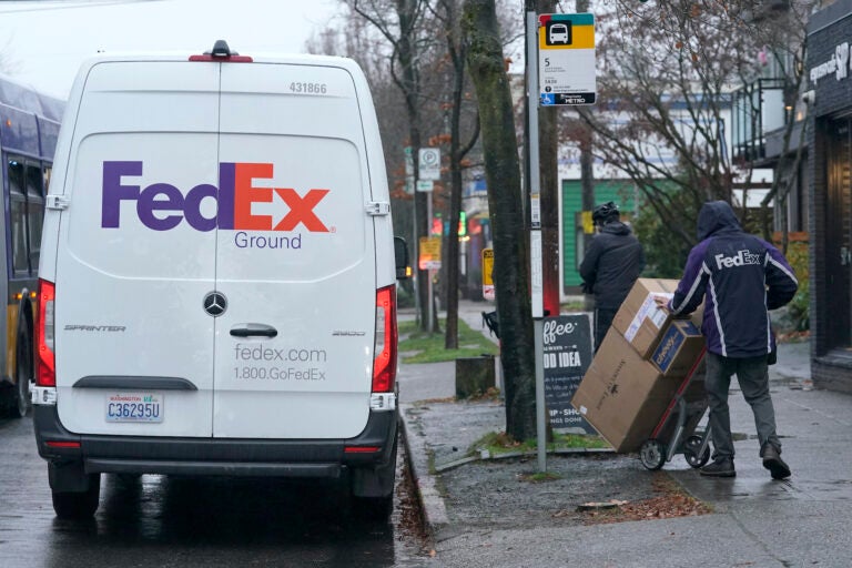 A driver with FedEx carries a package away from a van, Tuesday, Dec. 8, 2020, in Seattle. Store are warning online shoppers that if holiday purchases aren't made soon, they may not be delivered in time for Christmas. (AP Photo/Ted S. Warren)