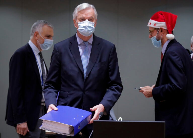 A colleague wears a Christmas hat as European Union chief negotiator Michel Barnier, center, carries a binder of the Brexit trade deal during a special meeting of Coreper, at the European Council building in Brussels, Friday, Dec. 25, 2020. (Olivier Hoslet, Pool via AP)