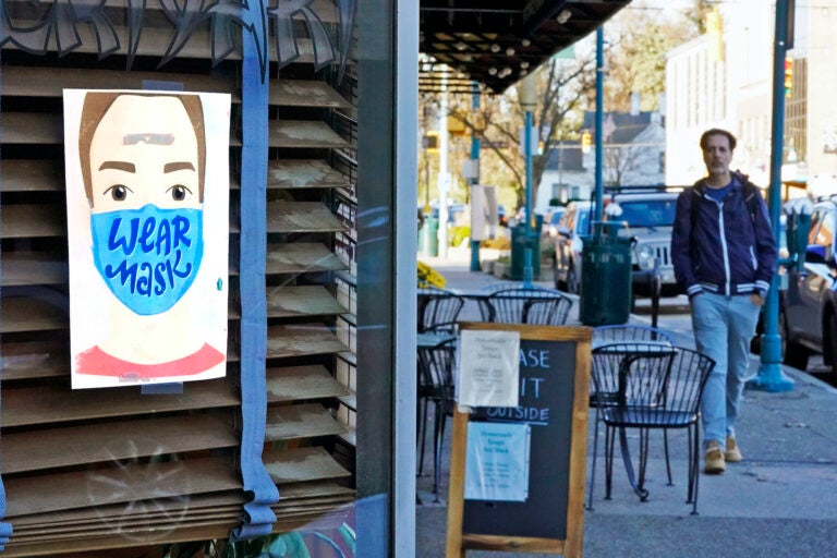 A man walks past a restaurant in Mount Lebanon, Pa., with a sign in the window that reminds people to wear a mask