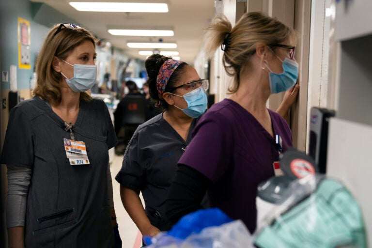 Registered nurse Kristina Shannon, from left, chaplain Andrea Cammarota, and ER charge nurse Cathy Carter watch as medical workers try to resuscitate a patient who tested positive for coronavirus in the emergency room