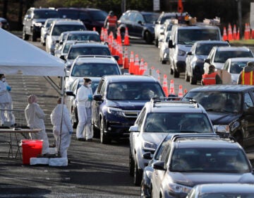 Staff at a drive-thru COVID-19 testing site talk to people waiting in line in their cars at the PNC Bank Arts Center