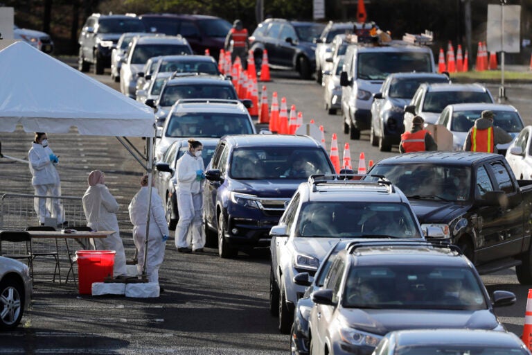 Staff at a drive-thru COVID-19 testing site talk to people waiting in line in their cars at the PNC Bank Arts Center