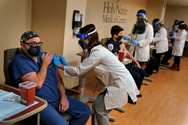 Nurse Reynaldo Pella, left, was one of five staff members to simultaneously receive the first doses of the COVID-19 vaccine